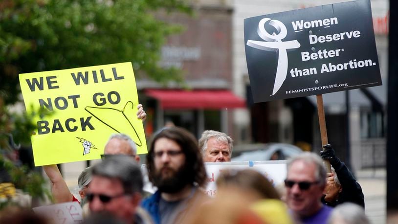 A pro-choice rally drew about 100 people to North Main Street in Dayton earlier this year. The group encouraged Premier Health to make a transfer agreement with Women’s Med Center, a move needed to keep the center open under to Ohio law. At right is an anti-abortion sign seen at the rally. TY GREENLEES / STAFF