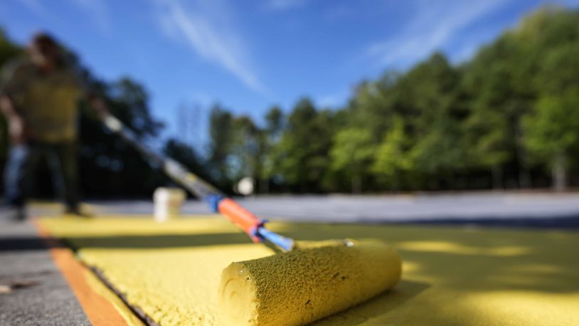 Ronnie Jefferies paints the parking lot at Science, Arts and Entrepreneurship School to help cool it by making it more reflective, Wednesday, Sept. 4, 2024, in Mableton, Ga. (AP Photo/Mike Stewart)